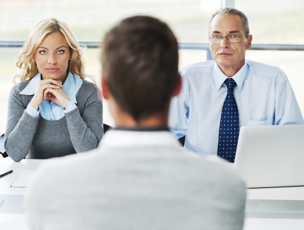 A picturte taken in a behavioral interview in a big corporation. A couple of HR managers sit opposite the job candidate. 