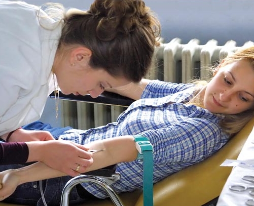 A phlebotomist takes blood from a young woman who lays on her back and tries to relax