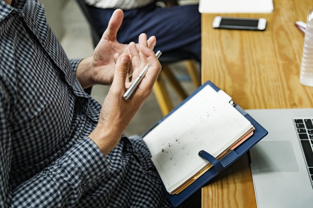 Man uses his hands to emphasize his words in a job interview. We can see his notebook on a table.